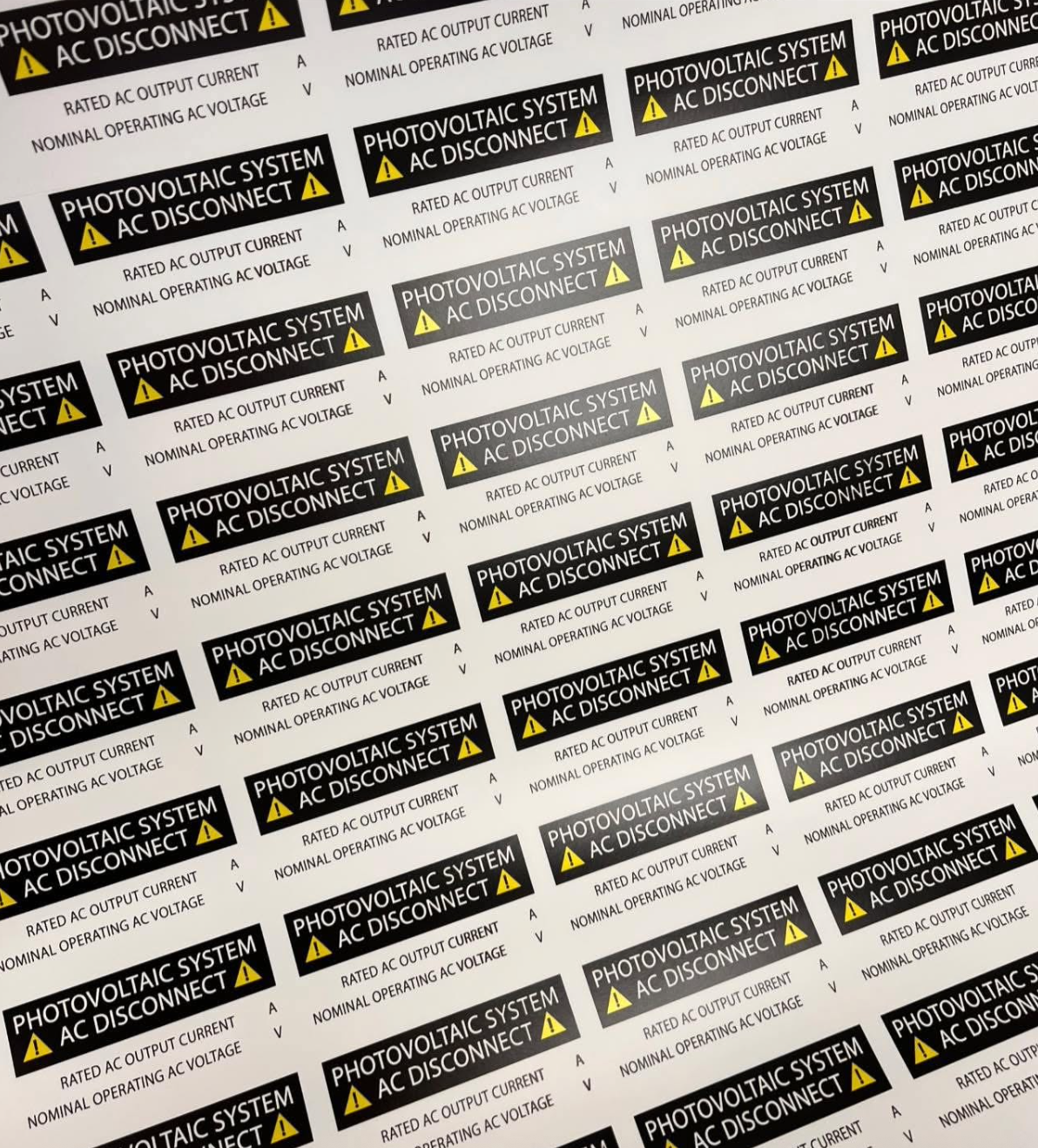 Full sheet of identical black and yellow Photovoltaic System AC Disconnect safety labels with blank fields for rated current and voltage, custom-printed by BAPS Signs & Wraps in Oldsmar, FL