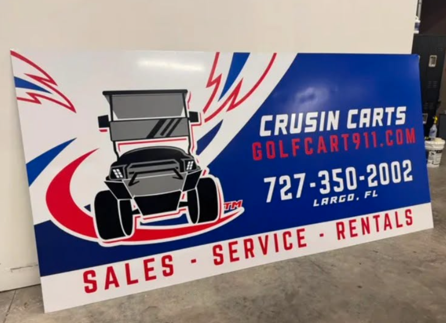 Large horizontal indoor promotional sign for Crusin Carts golf cart dealership with golf cart graphic, red and blue swooshes, website, phone number, and Sales Service Rentals text, produced by BAPS Signs & Wraps in Oldsmar, FL