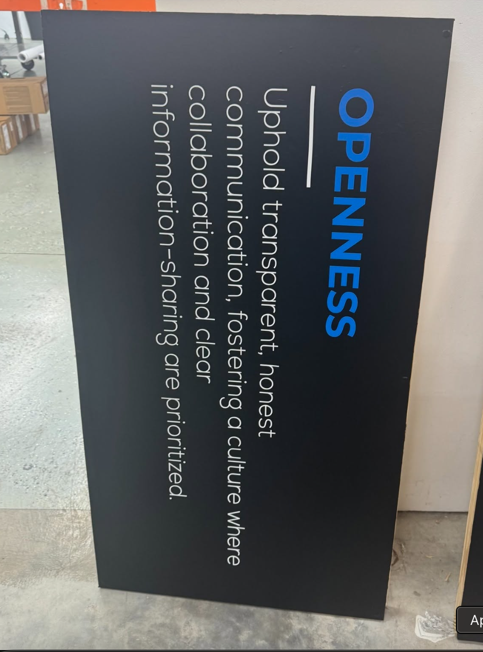Vertical indoor corporate values sign with bright blue OPENNESS heading and white body text on a dark charcoal background, produced by BAPS Signs & Wraps in Oldsmar, FL