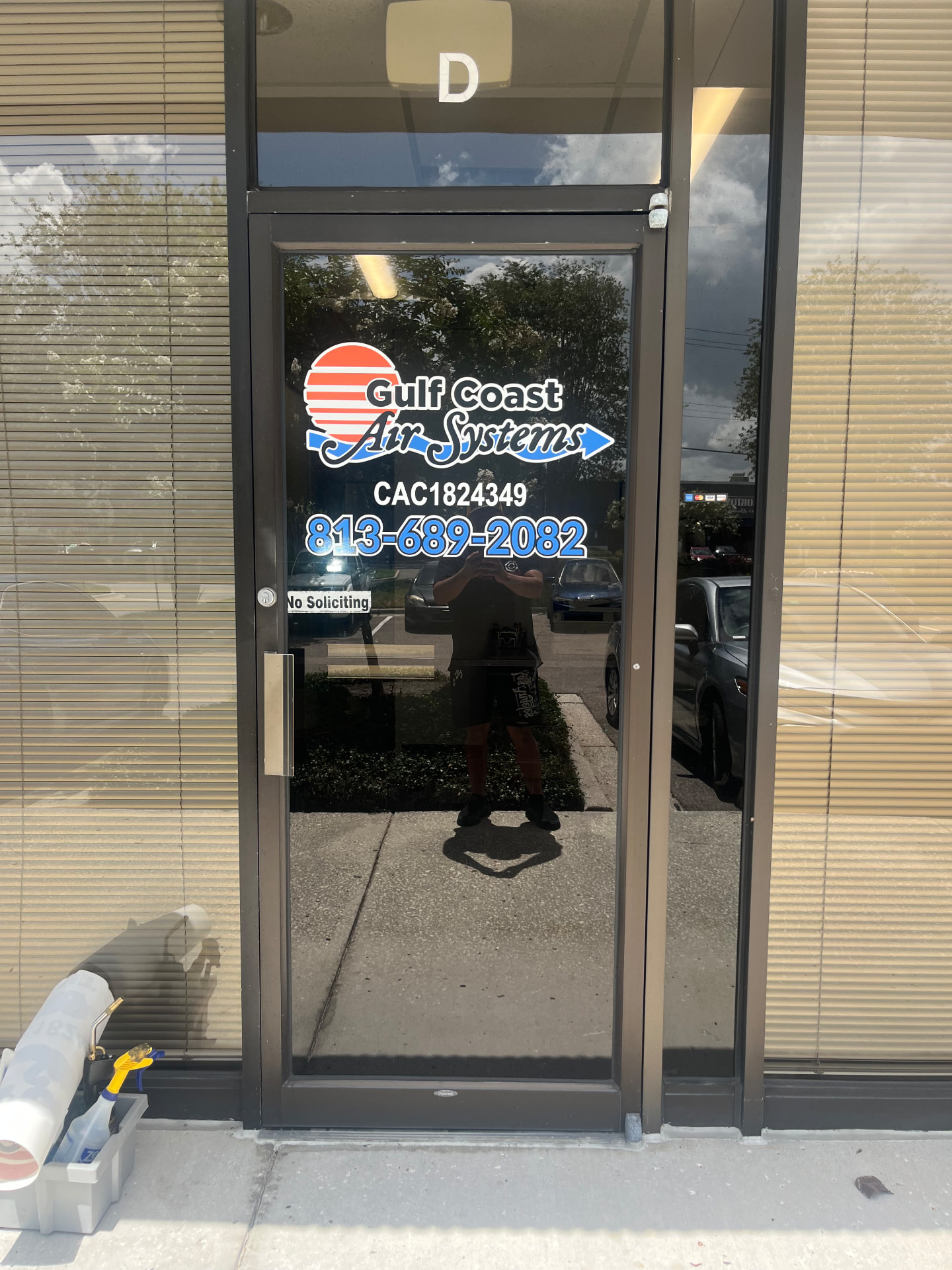 Storefront glass door with Gulf Coast Air Systems vinyl lettering, red and white sun logo, blue swoosh, phone number, and license number, installed by BAPS Signs & Wraps in Oldsmar, FL