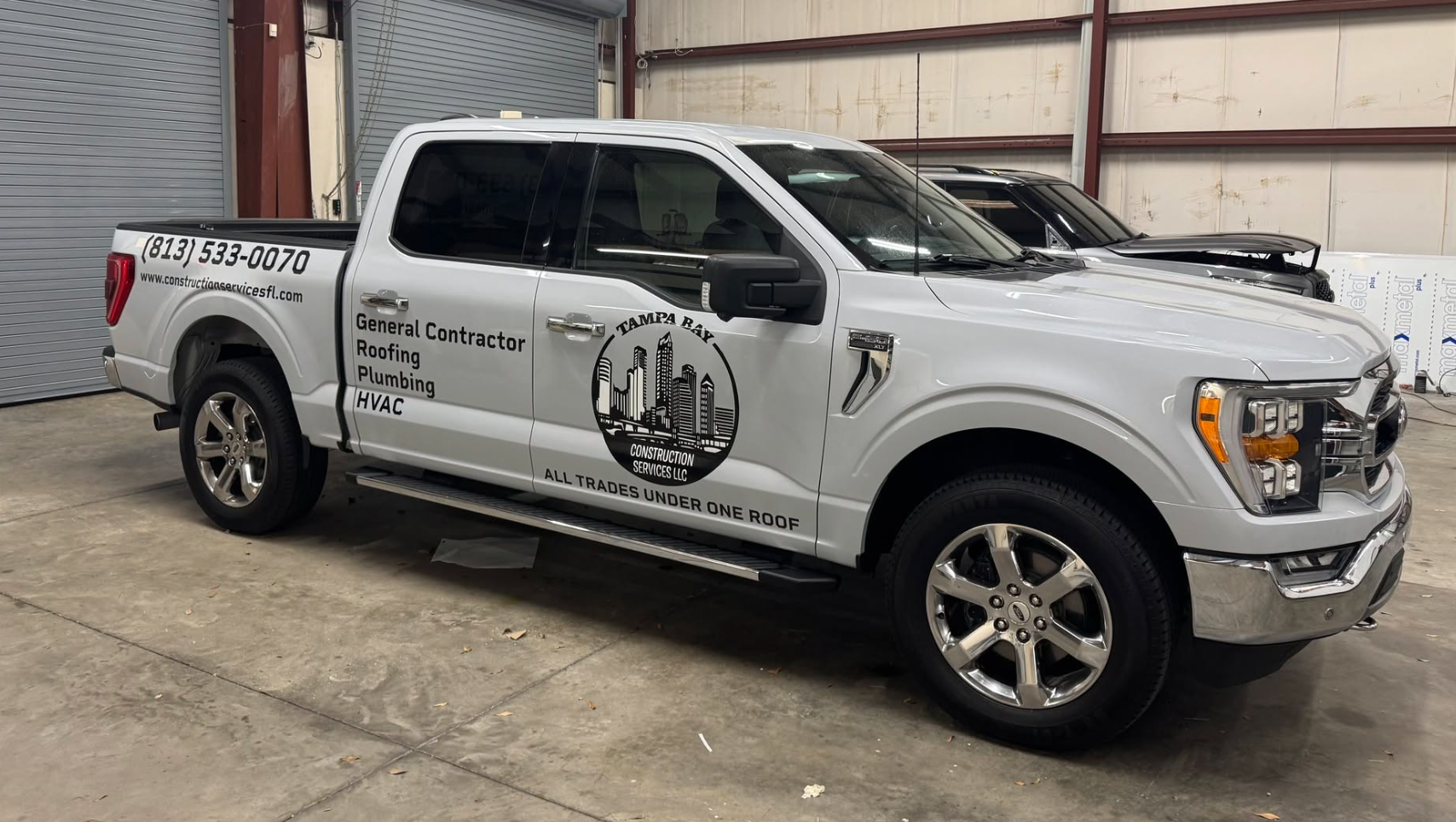 White Ford F-150 SuperCrew pickup truck with black Tampa Bay Construction Services LLC logo, service list, phone number, and website vinyl door decals, installed by BAPS Signs & Wraps in Oldsmar, FL